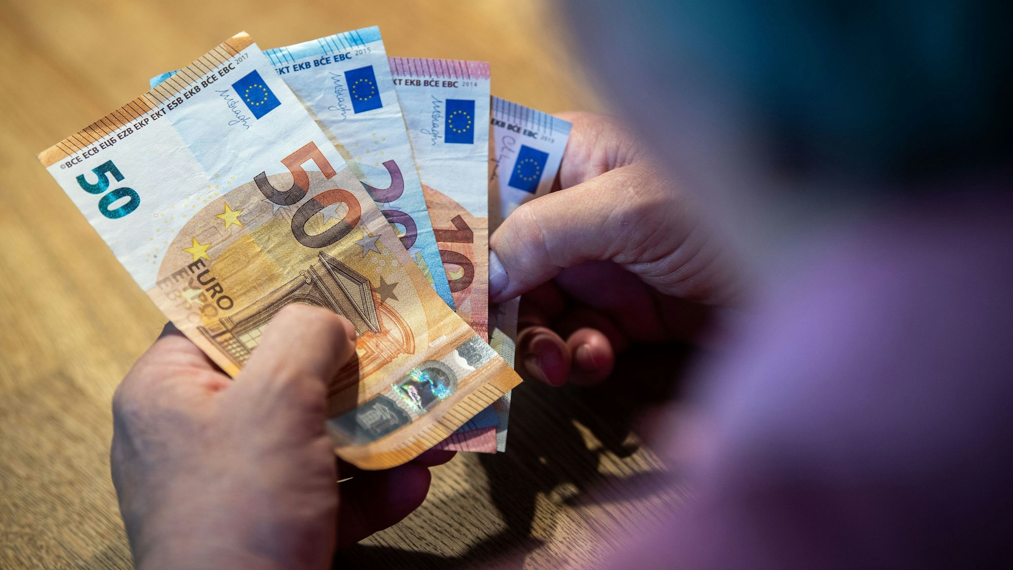 Ein älterer Mann sitzt an einem Tisch und zählt Geld.