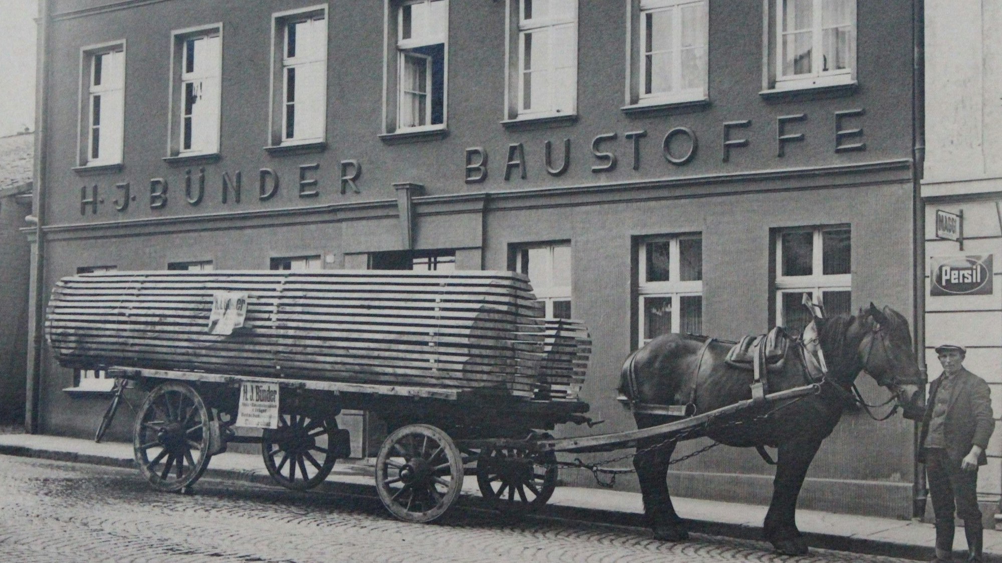 Das historische Foto zeigt ein Firmengebäude von Bünder in Euskirchen. Davor steht ein Wagen voller Bretter, der von einem Pferd gezogen wird.
