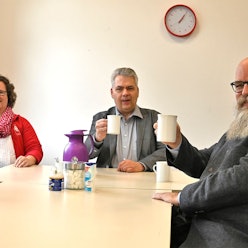 Drei Frauen und zwei Männer sitzen an einem Tisch und halten Tassen in den Händen.