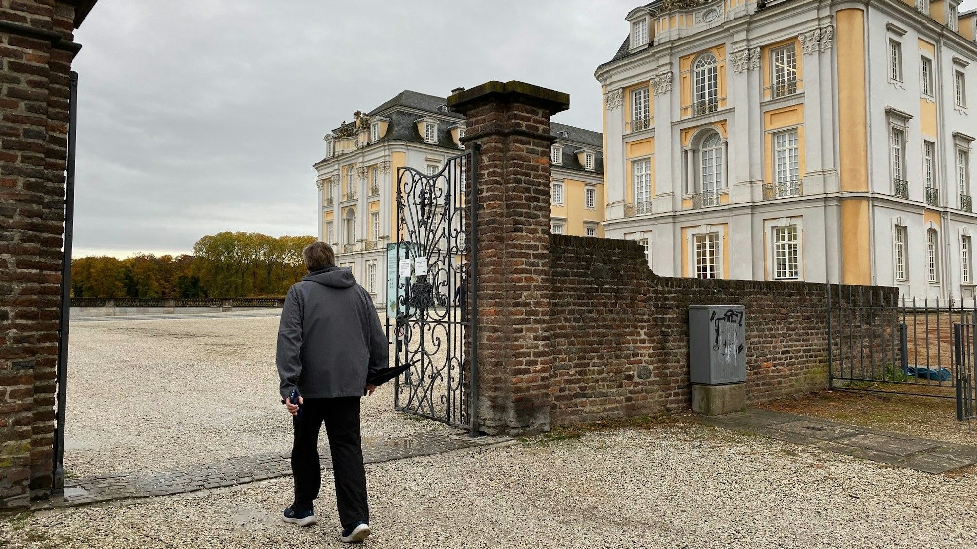 Zu sehen ist ein Spaziergänger, der den Park vor Schloss Augustusburg betritt.