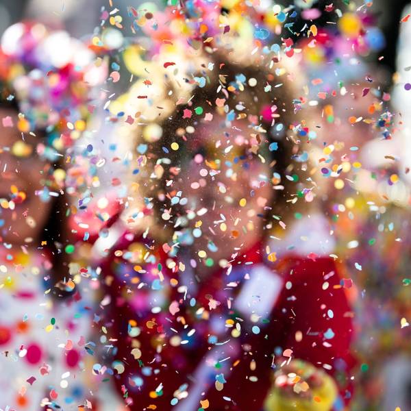 Konfetti fliegt vor bunt kostümierten Menschen durch die Luft.