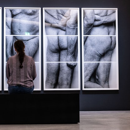 Eine Besucherin sitzt vor vier Fotografien des britischen Künstlers John Rivers Coplans