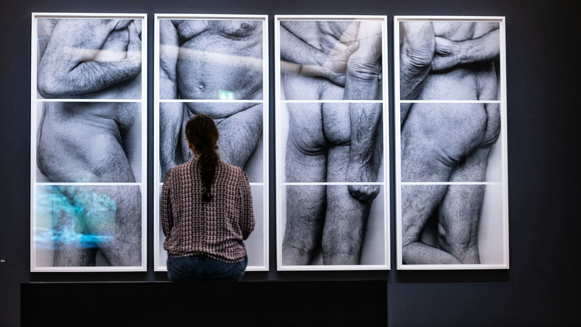 Eine Besucherin sitzt vor vier Fotografien des britischen Künstlers John Rivers Coplans