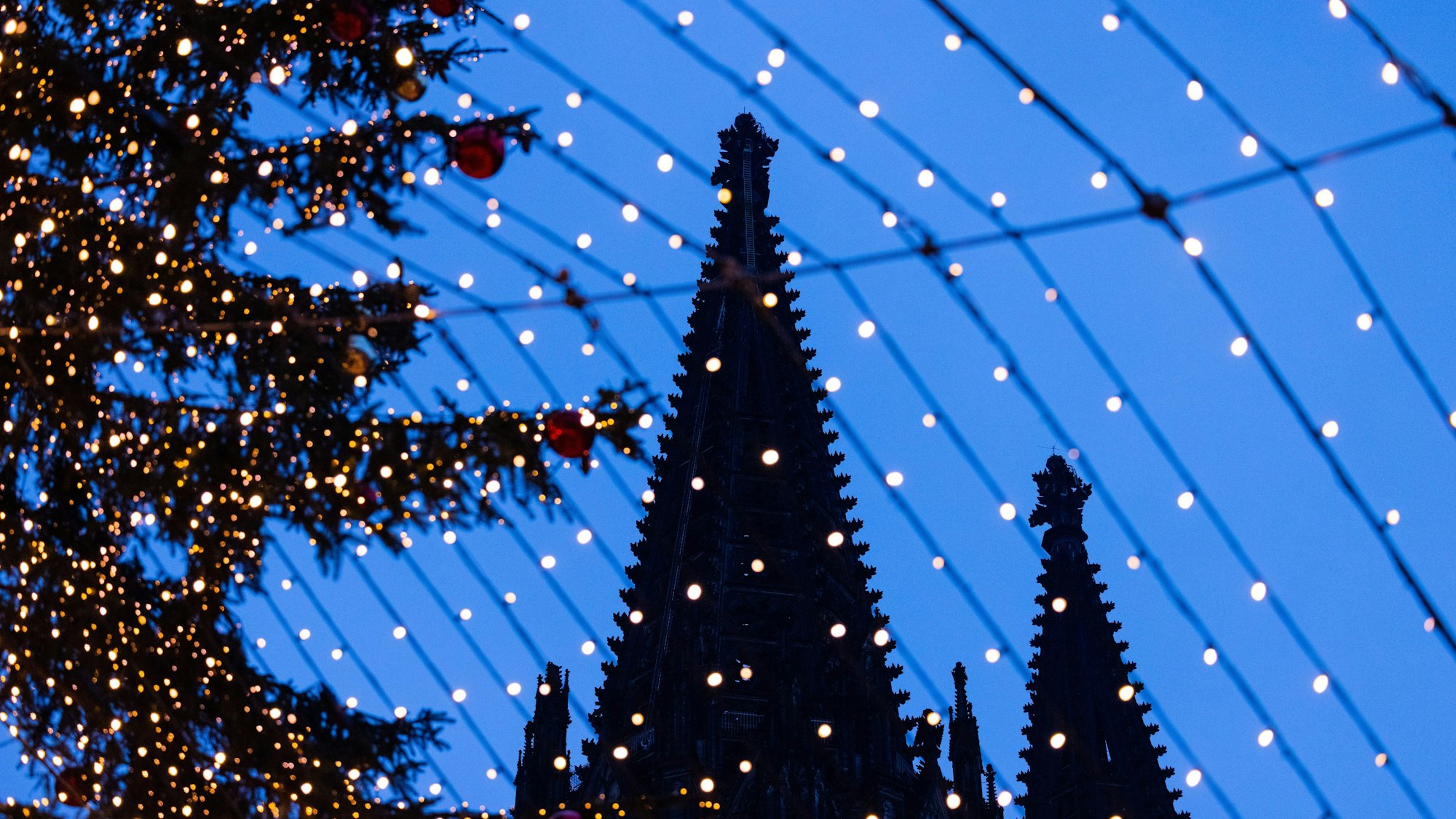 Köln: Die Domspitzen sind hinter Beleuchtung des Weihnachtsmarkts auf dem Roncalliplatz zu sehen.