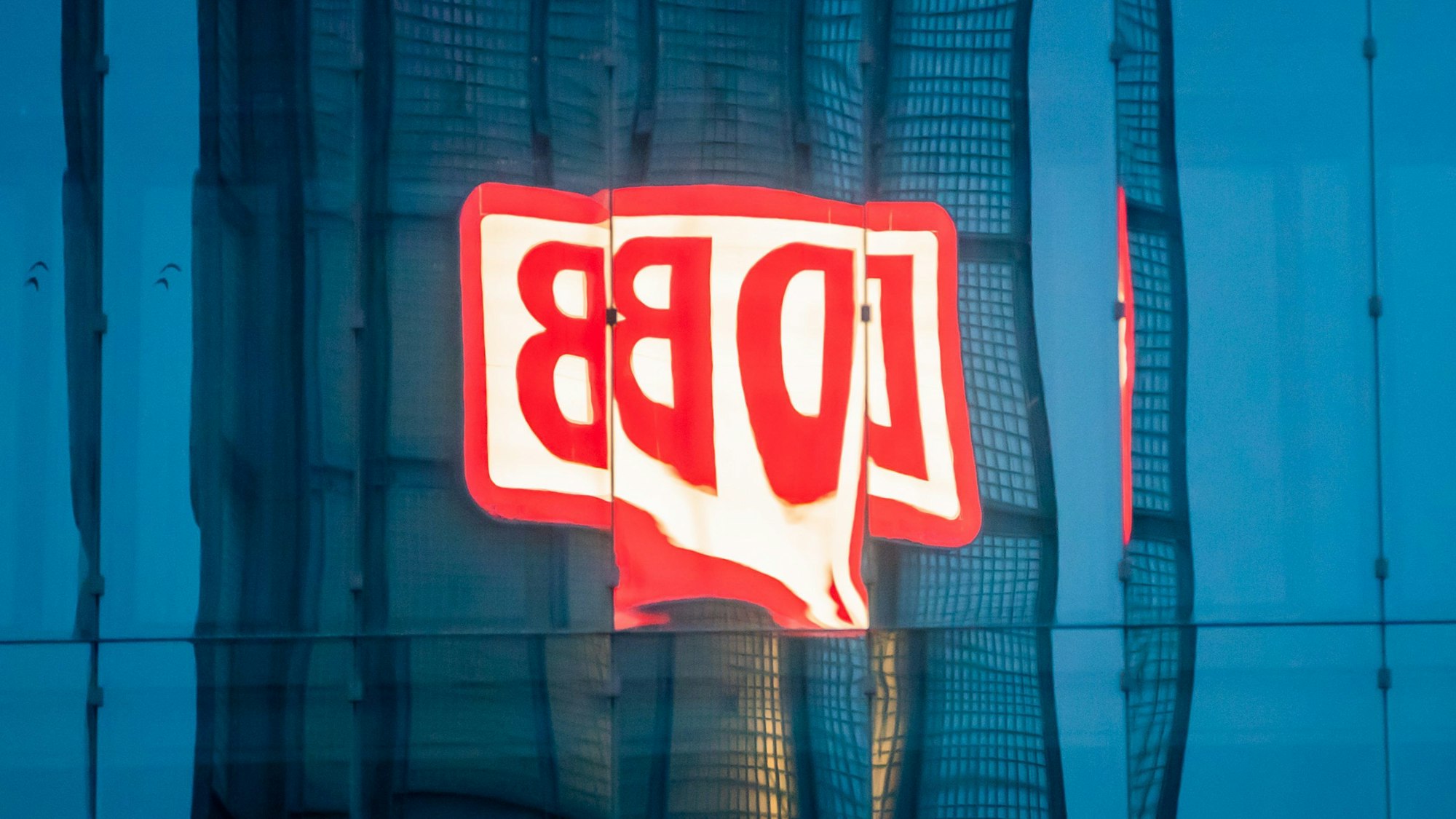 ARCHIV - 23.08.2021, Berlin: Das Logo der Deutschen Bahn AG (DB) am Berliner Hauptbahnhof spiegelt sich am Morgen in einer Gebäudefassade.