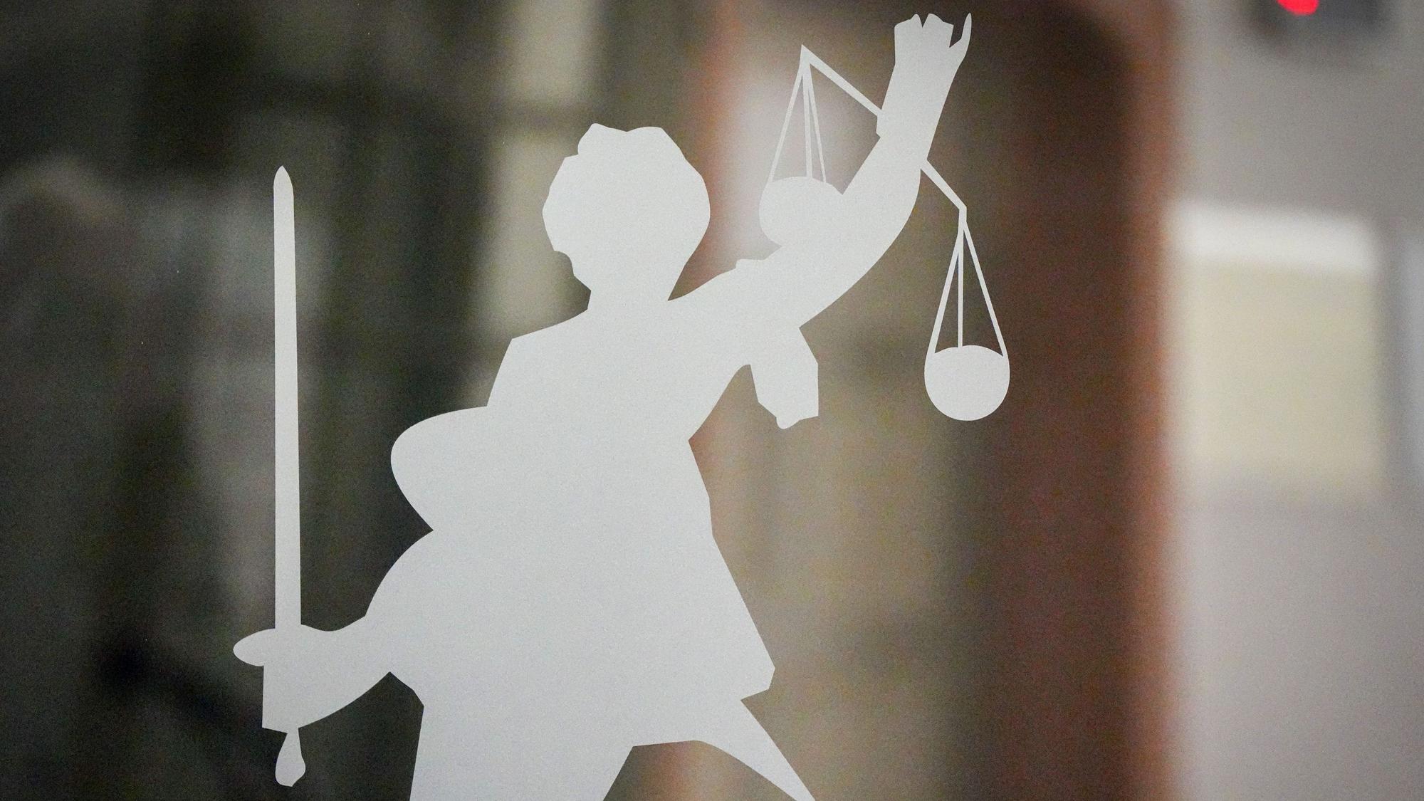 Die Figur der Justitia mit Richtschwert und Waage ist auf dem Glasfenster in einem Gerichtsgebäude zu sehen.