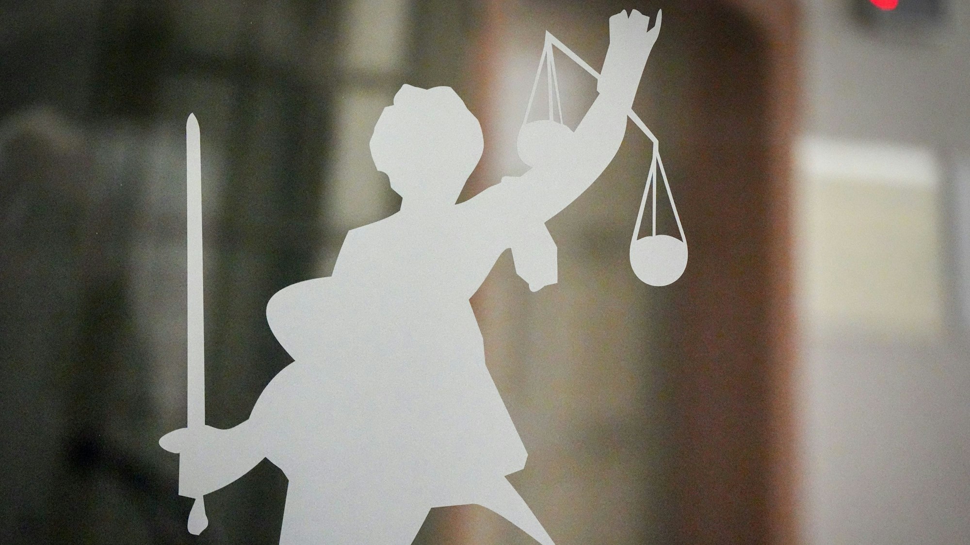 Die Figur der Justitia mit Richtschwert und Waage ist auf dem Glasfenster in einem Gerichtsgebäude zu sehen.