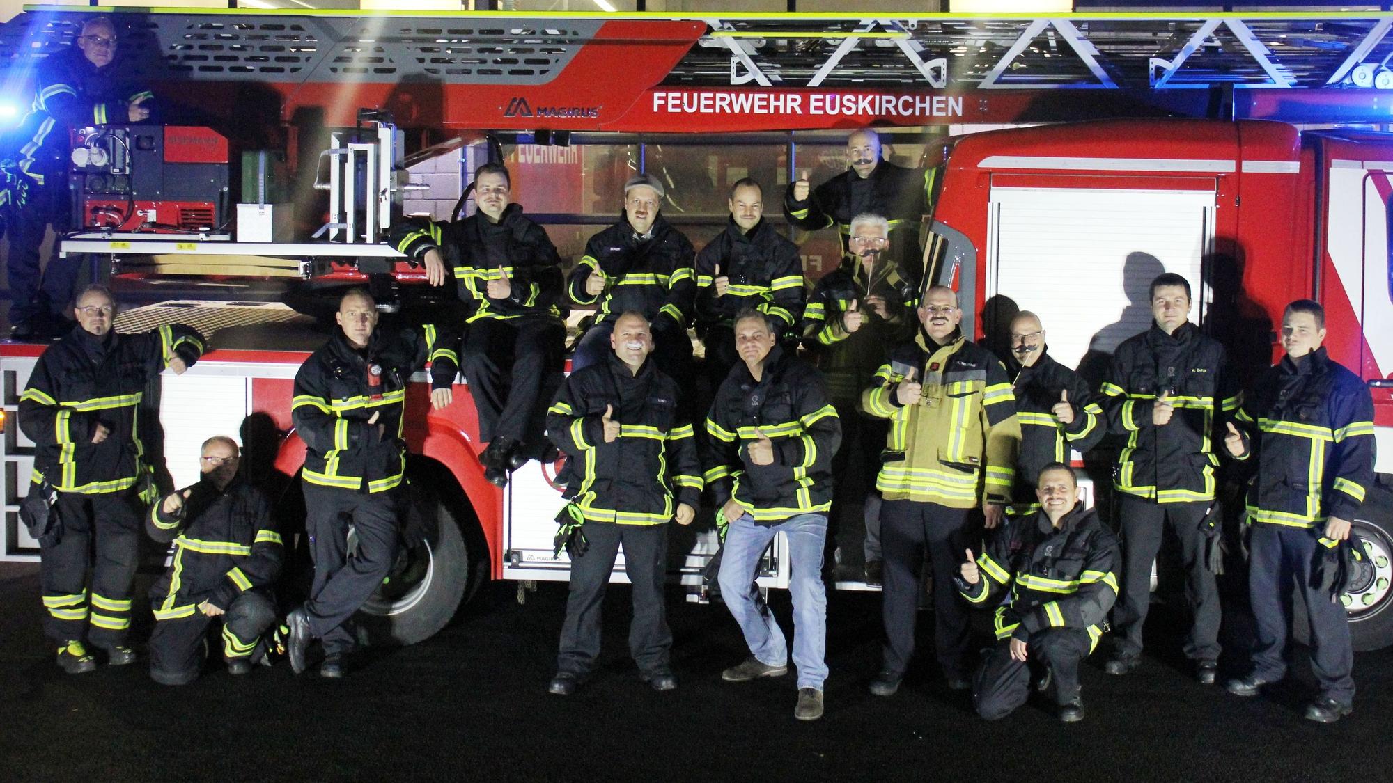 Mitglieder der Feuerwehr Euskirchen und Vertreter der Stadtverwaltung stehen vor einem Feuerwehrwagen. Sie tragen Schnurrbärte als Zeichen der Unterstützung für die Initiative Movember.