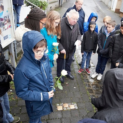 Alois Sommer mit einer Gruppe von Schulkindern. Einige tragen eine weiße Rose in der Hand.