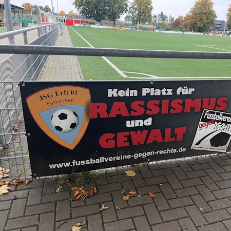 Das Bild zeigt ein Schild mit der Aufschrift „Kein Platz für Rassismus und Gewalt“ auf dem Sportplatz der JSG Erft in Kuchenheim.