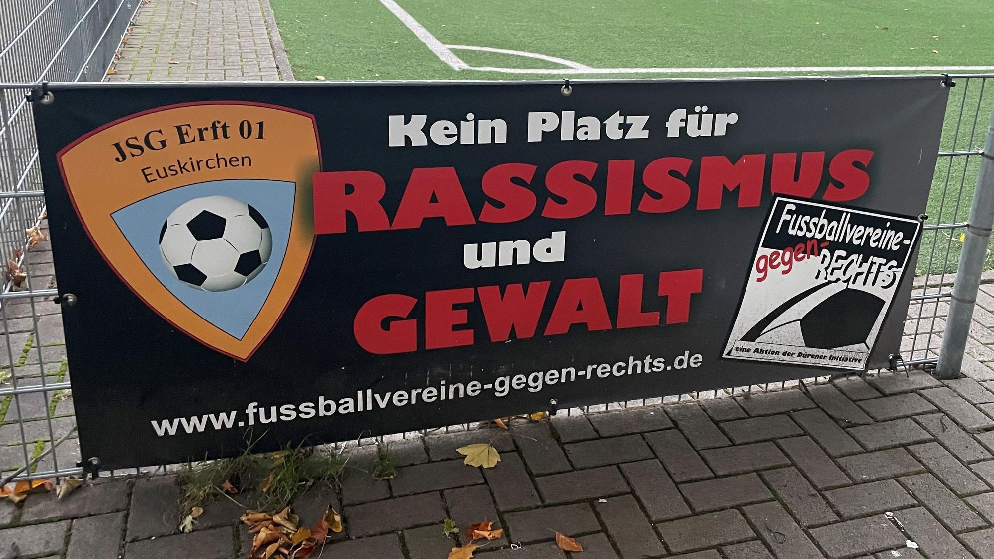 Das Bild zeigt ein Schild mit der Aufschrift „Kein Platz für Rassismus und Gewalt“ auf dem Sportplatz der JSG Erft in Kuchenheim.