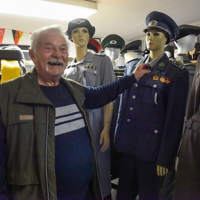 Das Foto zeigt Armin Schmitt vor Uniformen aus der ehemaligen DDR.