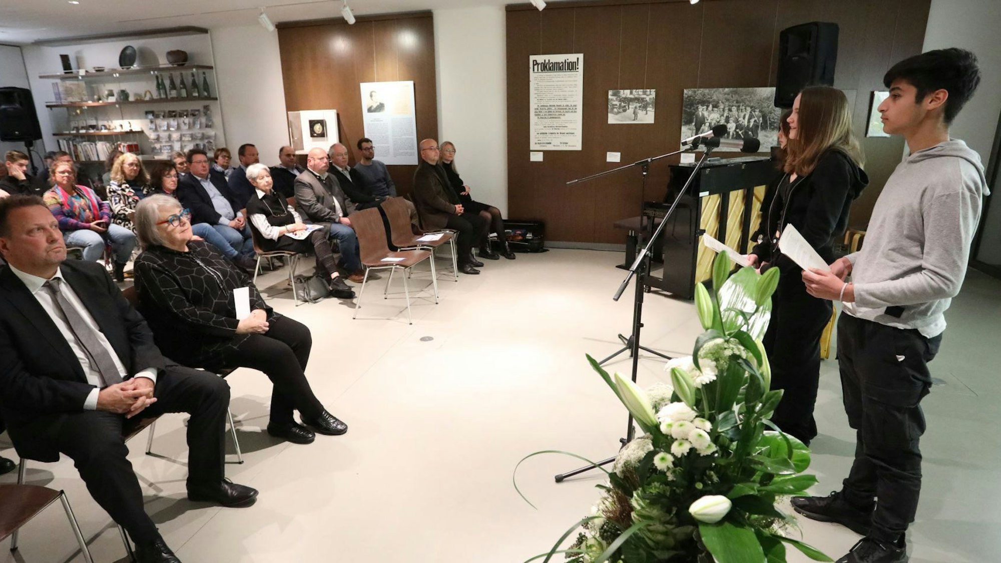 Zwei Schüler stehen an Mikrofonen im Foyer des Siebengebirgsmuseums; unter den Zuhörern ist Bürgermeister Lutz Wagner.