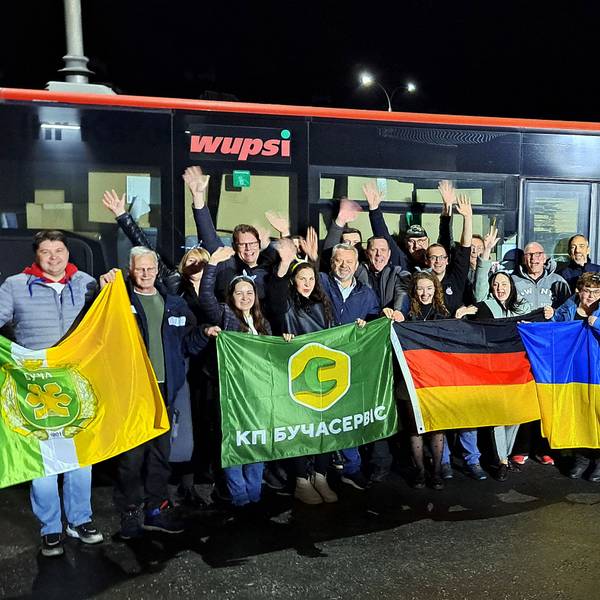 Menschen mit Fahnen stehen am Abend vor einem Linienbus.