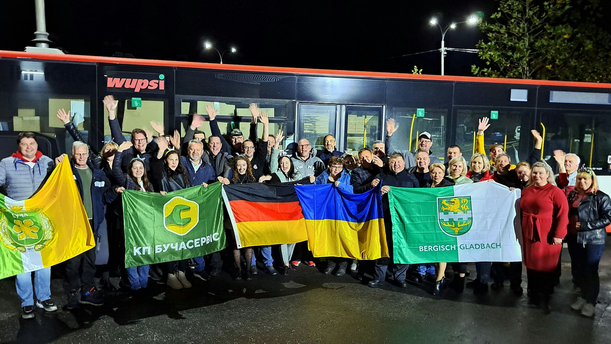 Menschen mit Fahnen stehen am Abend vor einem Linienbus.