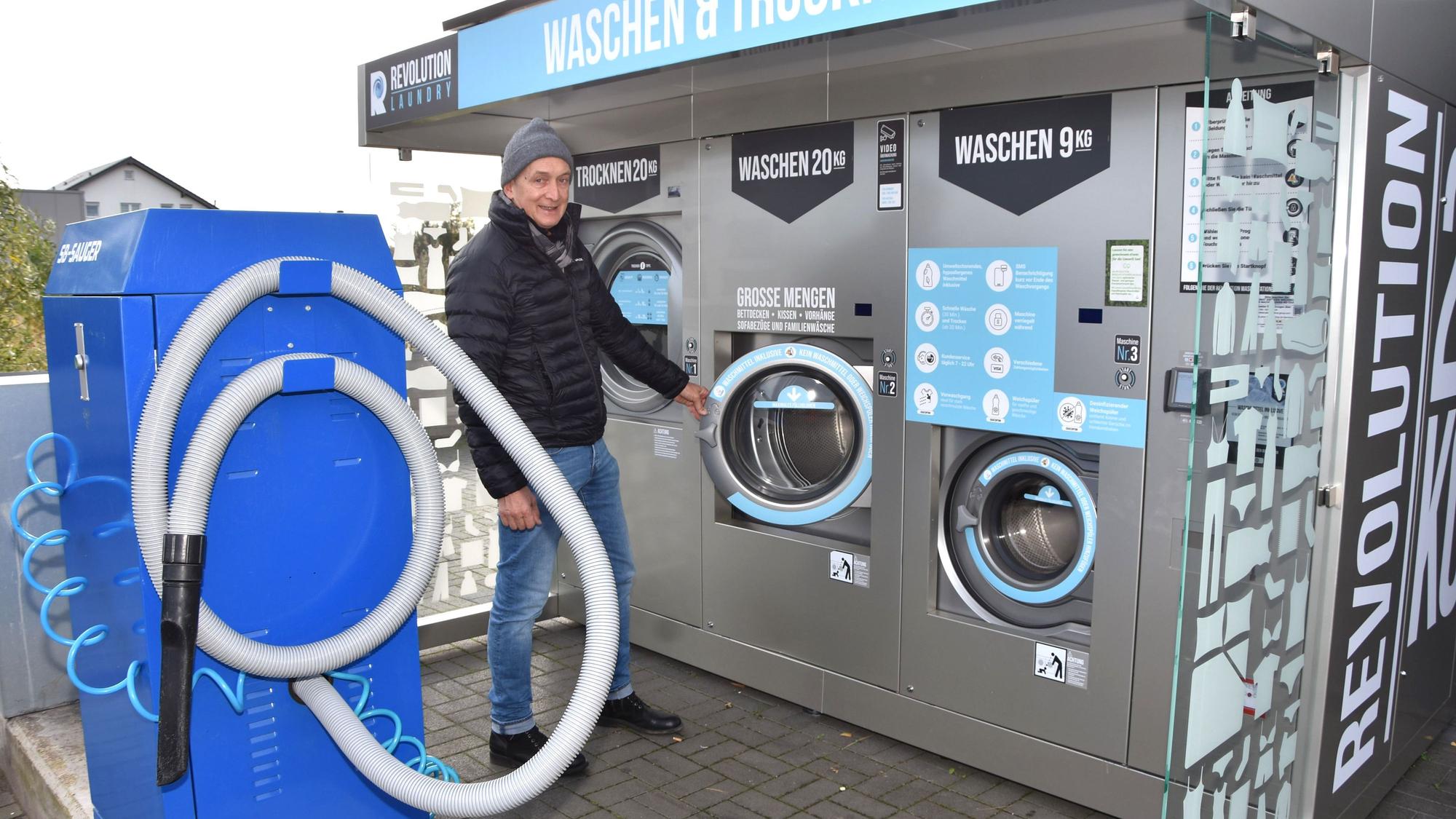 Ein Mann mit Mütze steht zwischen einem großen Autostaubsauger und großen Waschautomaten.