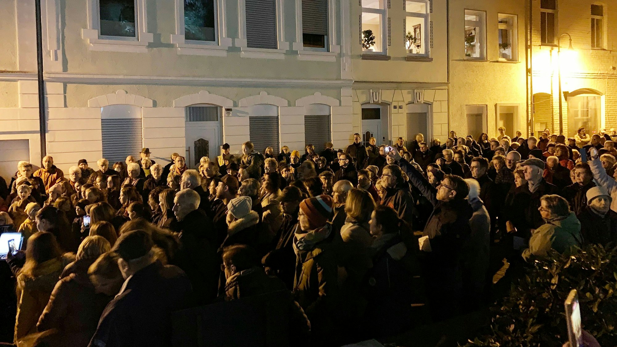 Eine Menschenmenge steht bei Dunkelheit in der Annaturmstraße, im Hintergrund Häuser mit erleuchteten Zimmern.