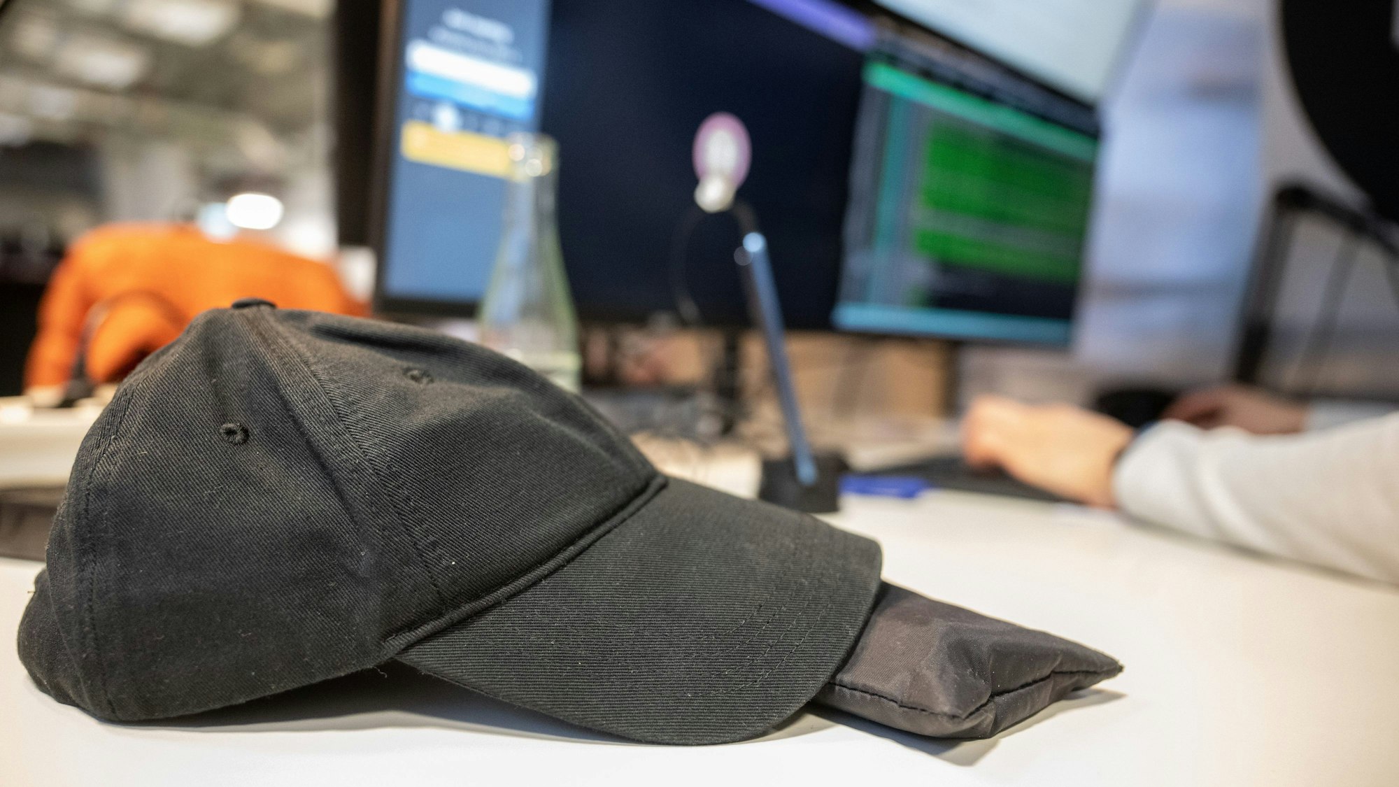Eine Baseballmütze liegt in einem Coworking-Space auf dem Tisch eines Programmierers.