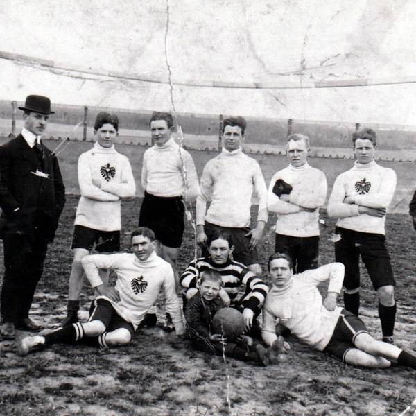 Eine alte Schwarz-Weiß-Fotografie zeigt Fußballer in Trikots und Männer mit Anzug und Melonen-Hüten.