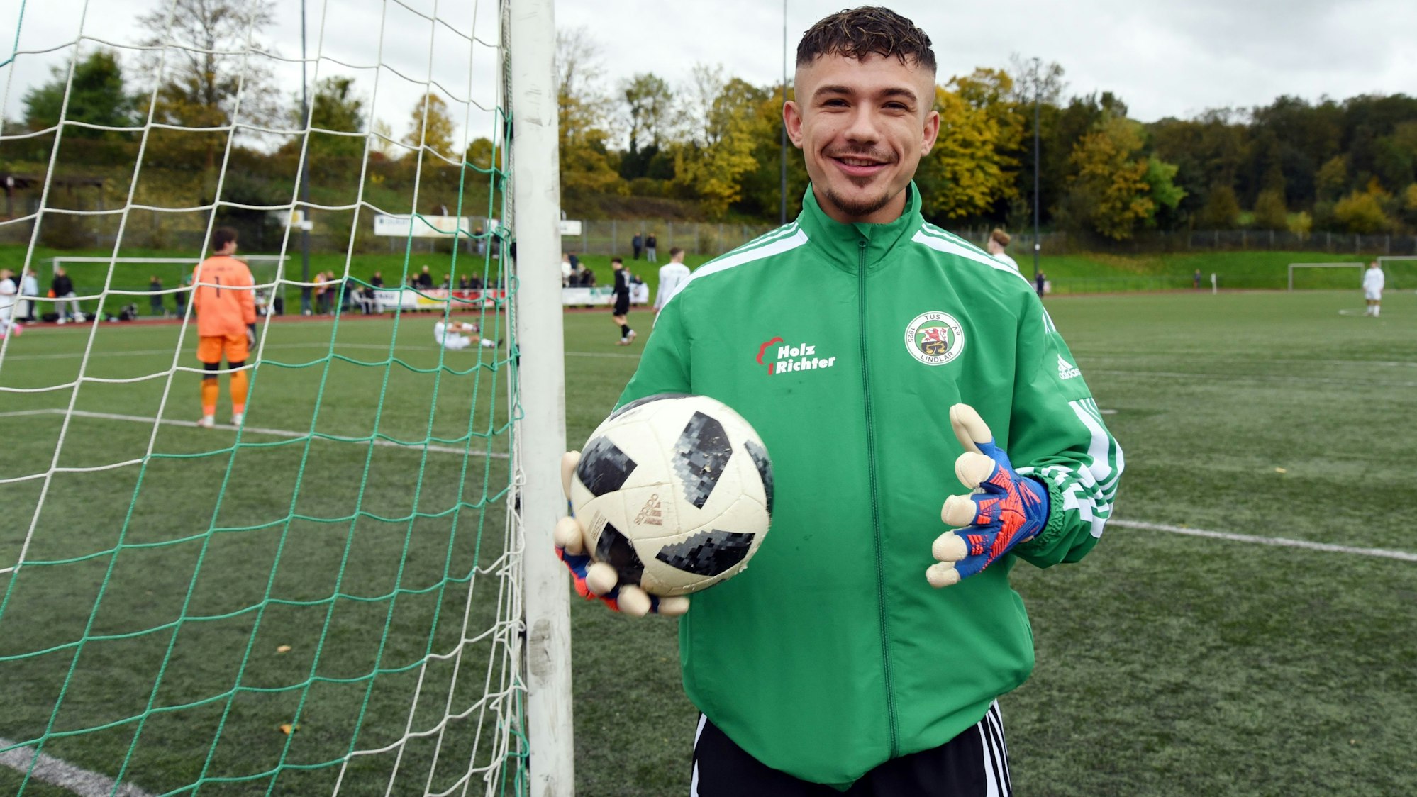 Ein Fußballspieler steht mit Torwarthandschuhen und Ball an einem Tor.