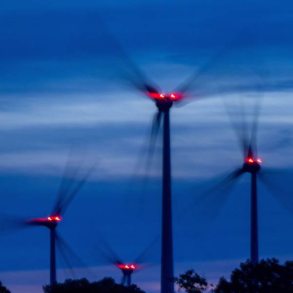 Mit Signallampen beleuchtete Windräder drehen sich nach Sonnenuntergang in einem Windpark.