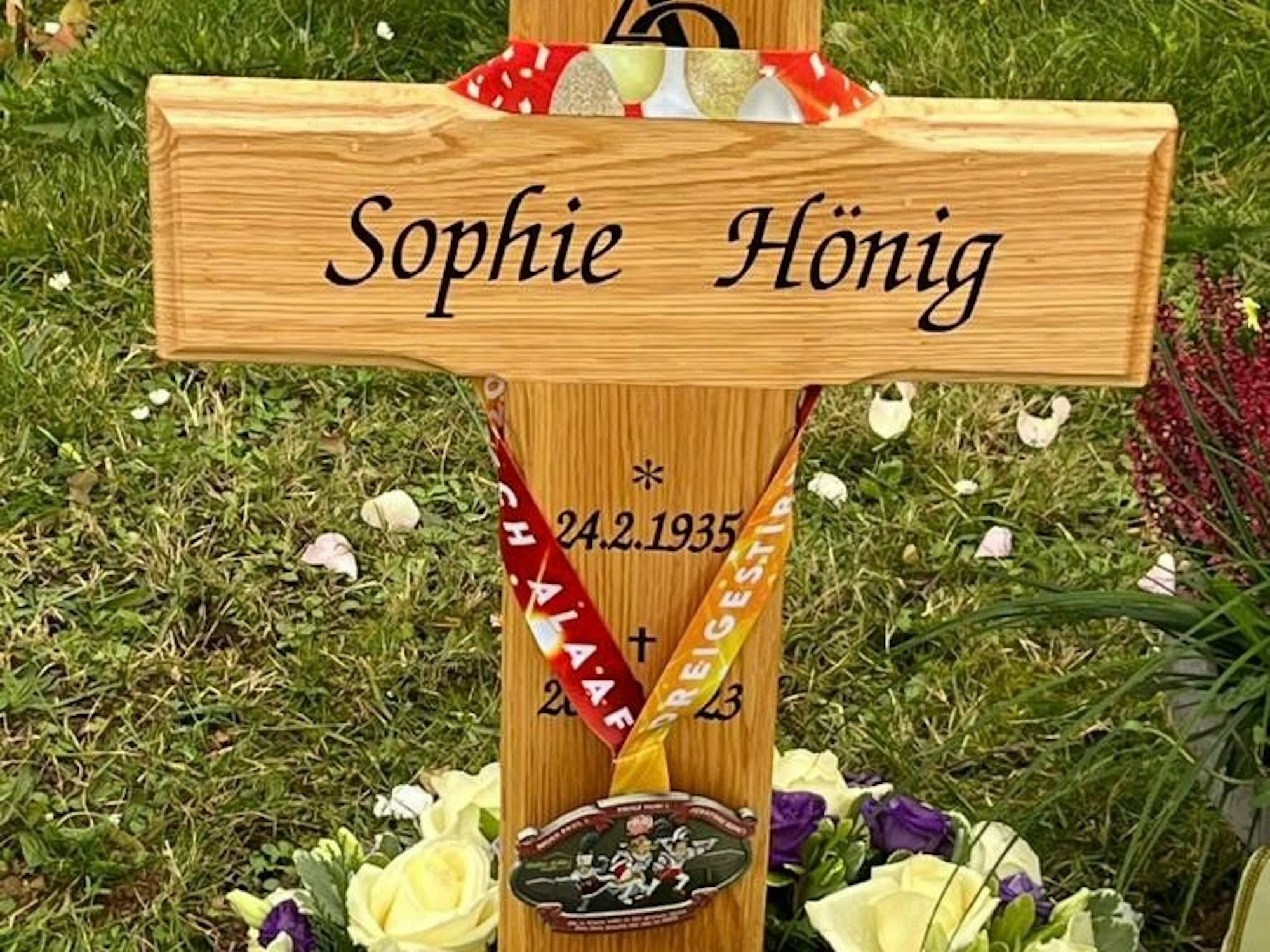 Das Bild zeigt ein Holzkreuz, an dem ein Karnevalsorden hängt.