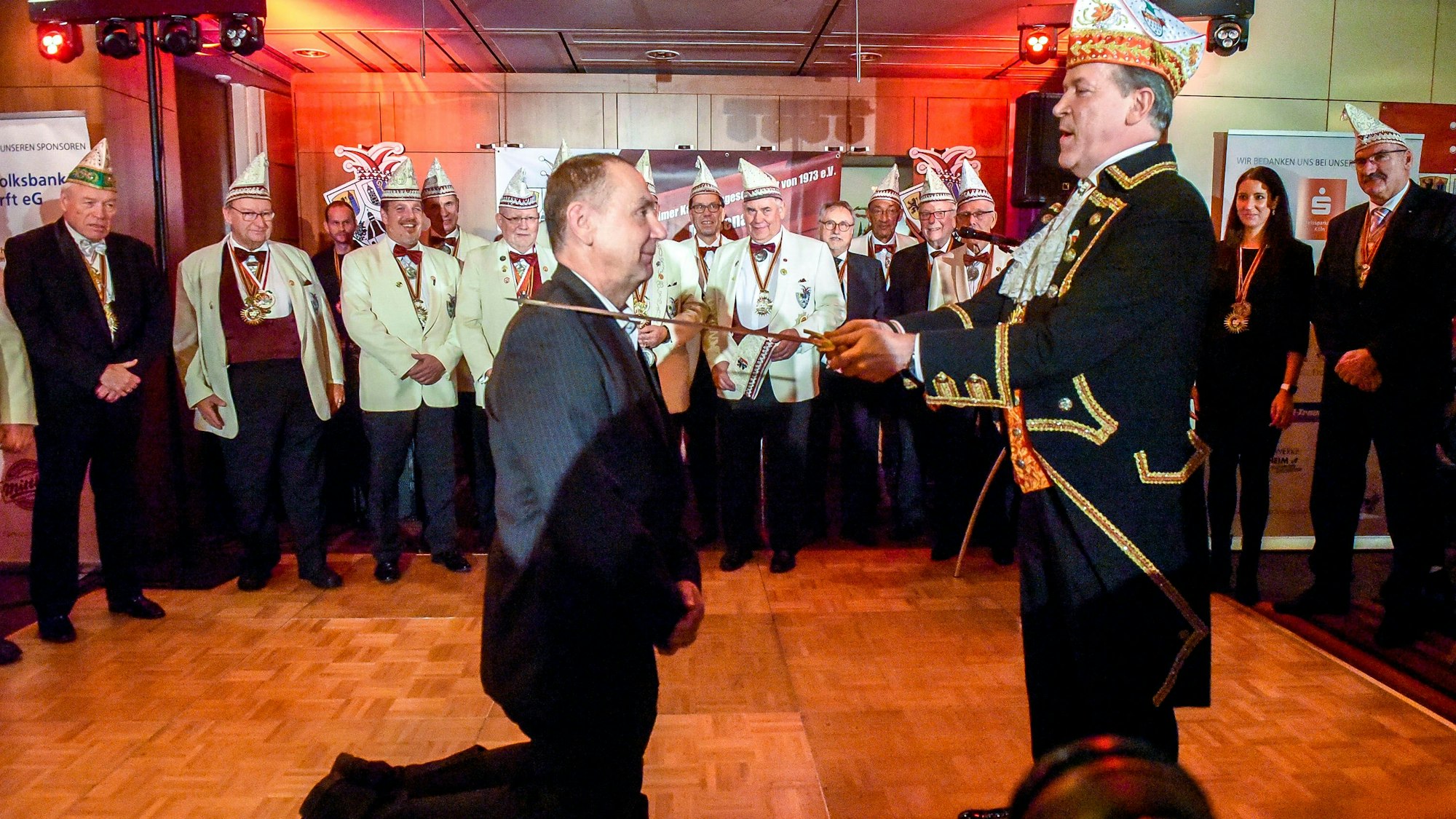 Ein Mann kniet, ein anderer berührt ihn mit einem Schert an der Schulter.