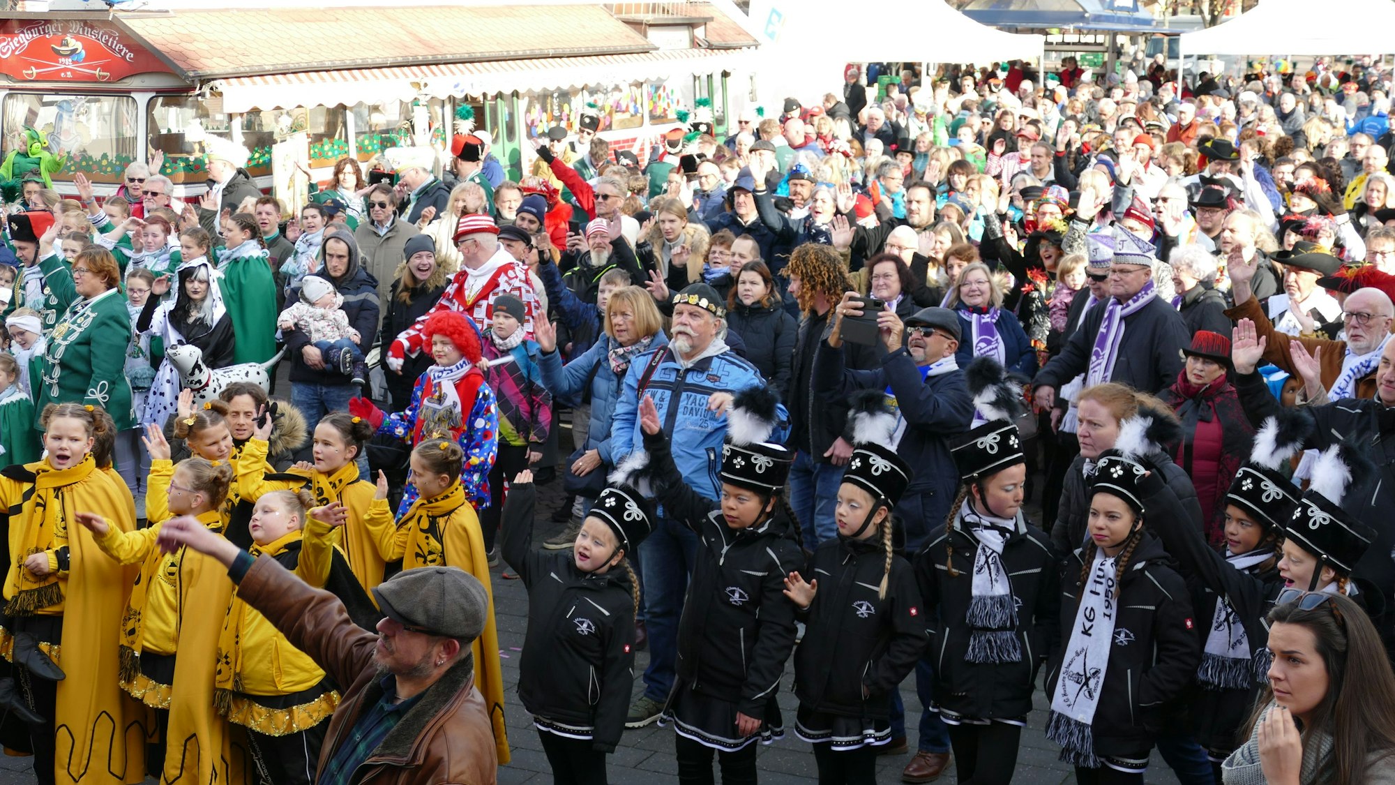 Kinder und Erwachsene stehen in einer großen Menge auf dem Siegburger Markt. Sie tragen Uniformen ihrer Karnevalsgesellschaften in vielen Farben.