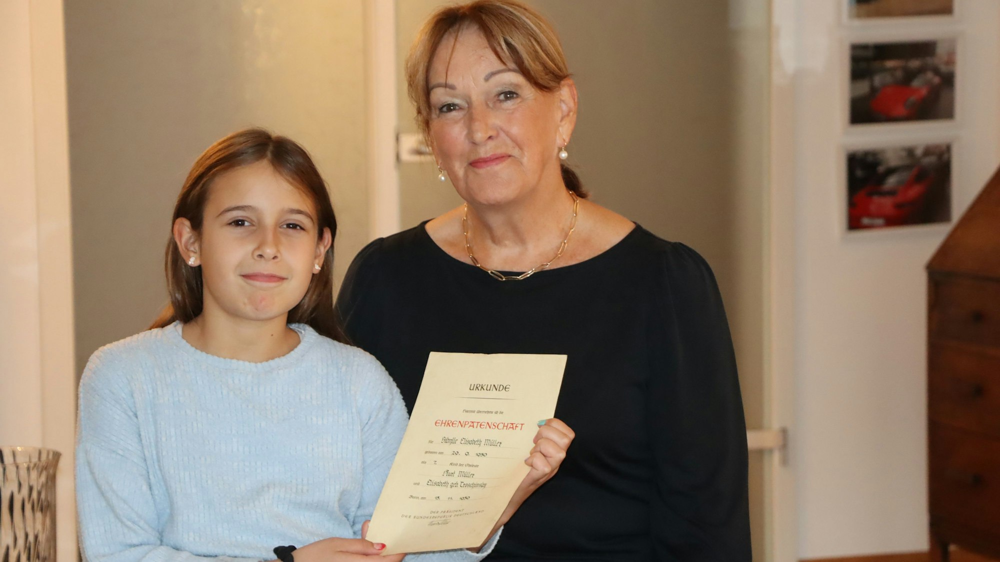 Ein junges Mädchen und ihre Oma zeigen die gut erhaltene Urkunde über die Ehrenpatenschaft.