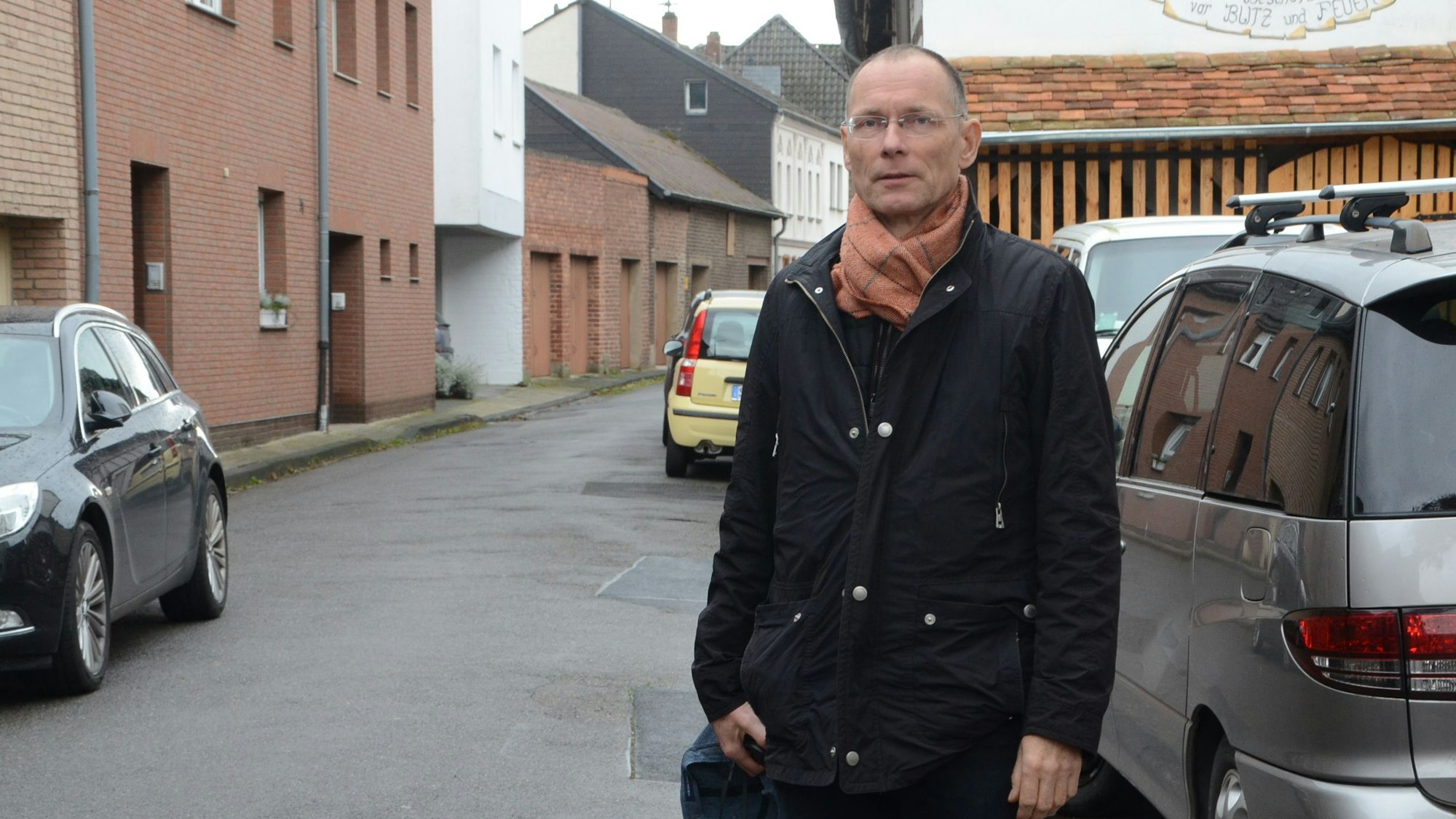 Ein Mann steht auf einer engen Straße. Die Gehwege sind sehr schmal, links und rechts parken Autos.