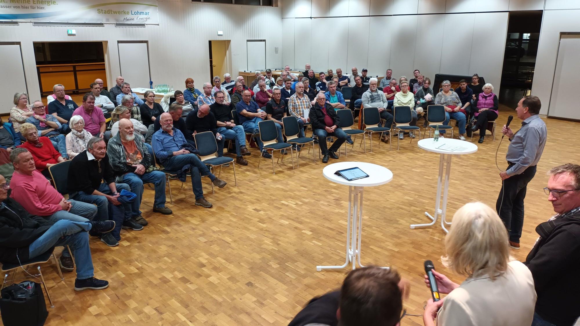 Bürgerinnen und Bürger sitzen bei einer Versammlung in einem Saal.