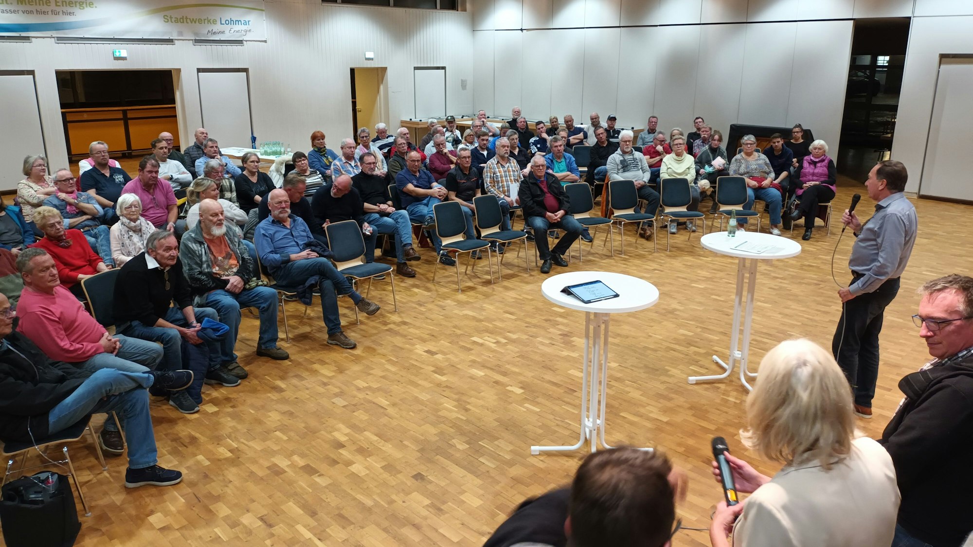 Bürgerinnen und Bürger sitzen bei einer Versammlung in einem Saal.