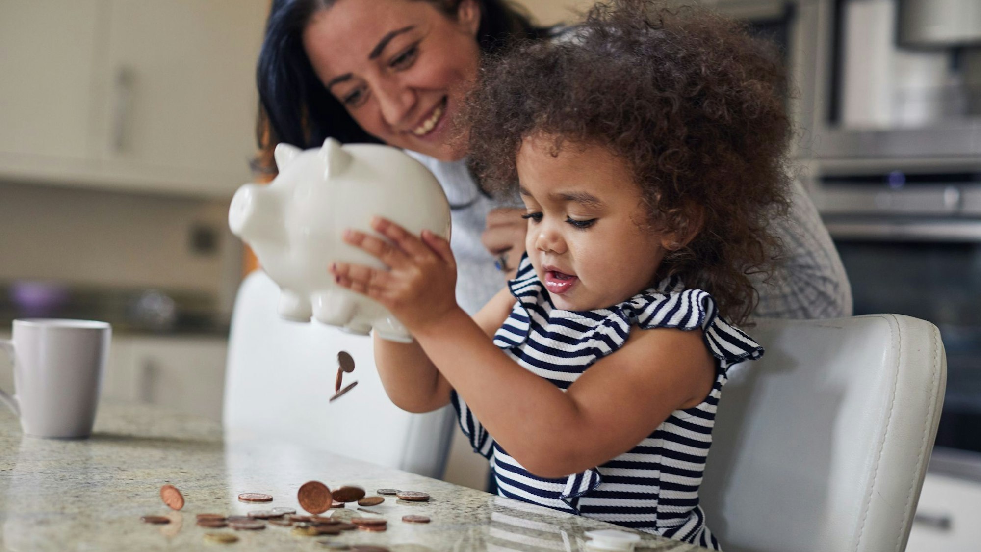 Ein kleines Mädchen leert zusammen mit der Mutter sein Sparschwein aus.