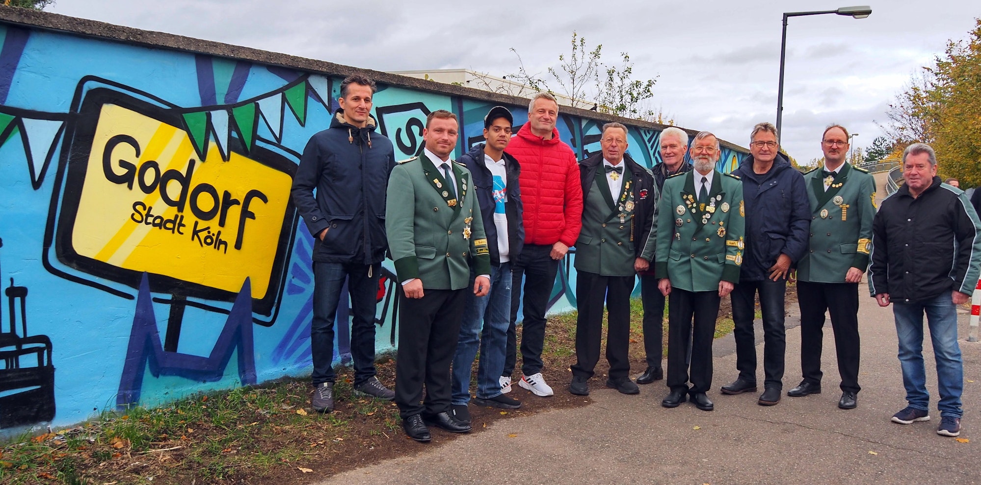 Männer und Jugendliche stehen teils in Schützen-Uniform neben einer frisch mit Graffiti besprühten Mauer.