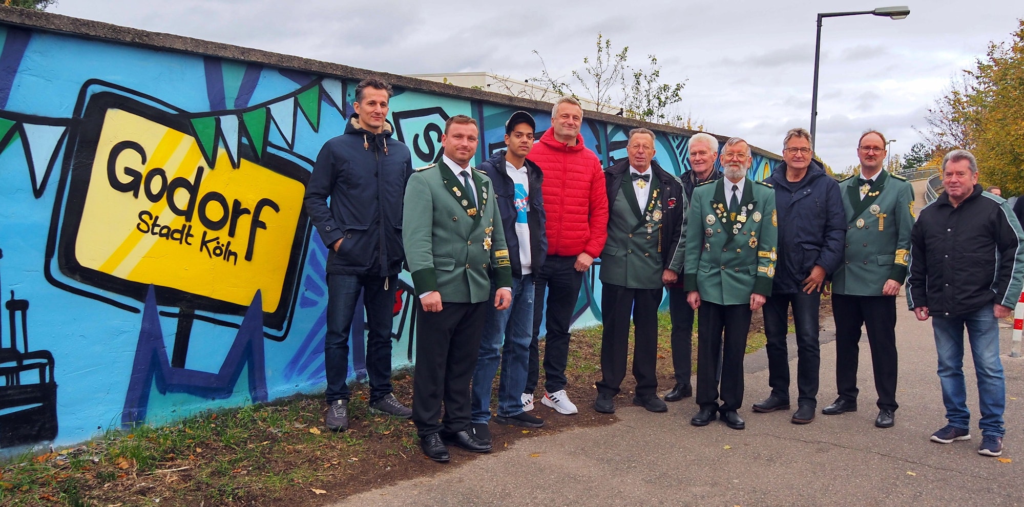 Männer und Jugendliche stehen teils in Schützen-Uniform neben einer frisch mit Graffiti besprühten Mauer.