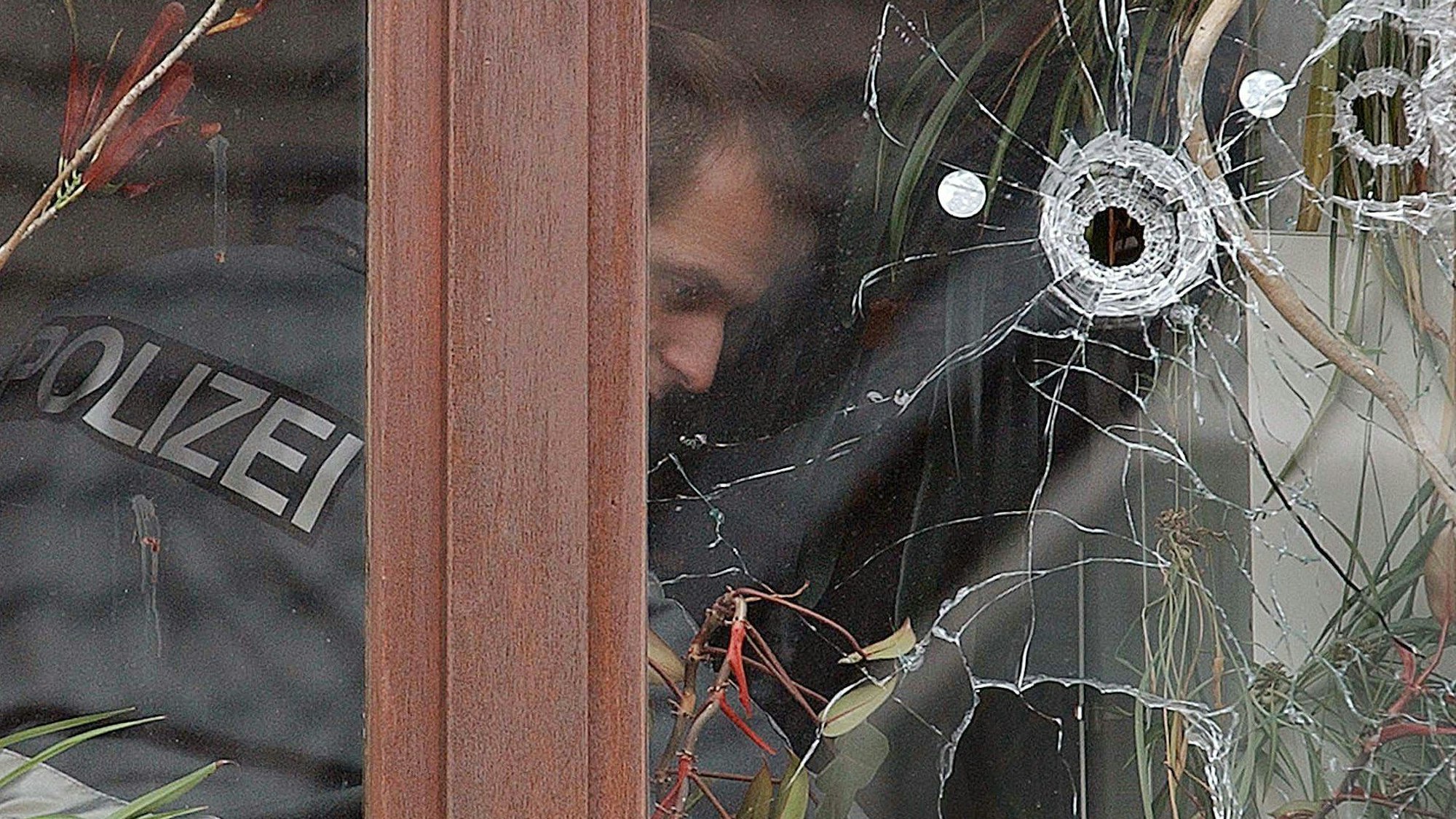 Ein Kriminalbeamter schaut sich Einschusslöcher in einer Scheibe einer Anwaltskanzlei in Overath an ( Archivfoto vom 08.10.2003).