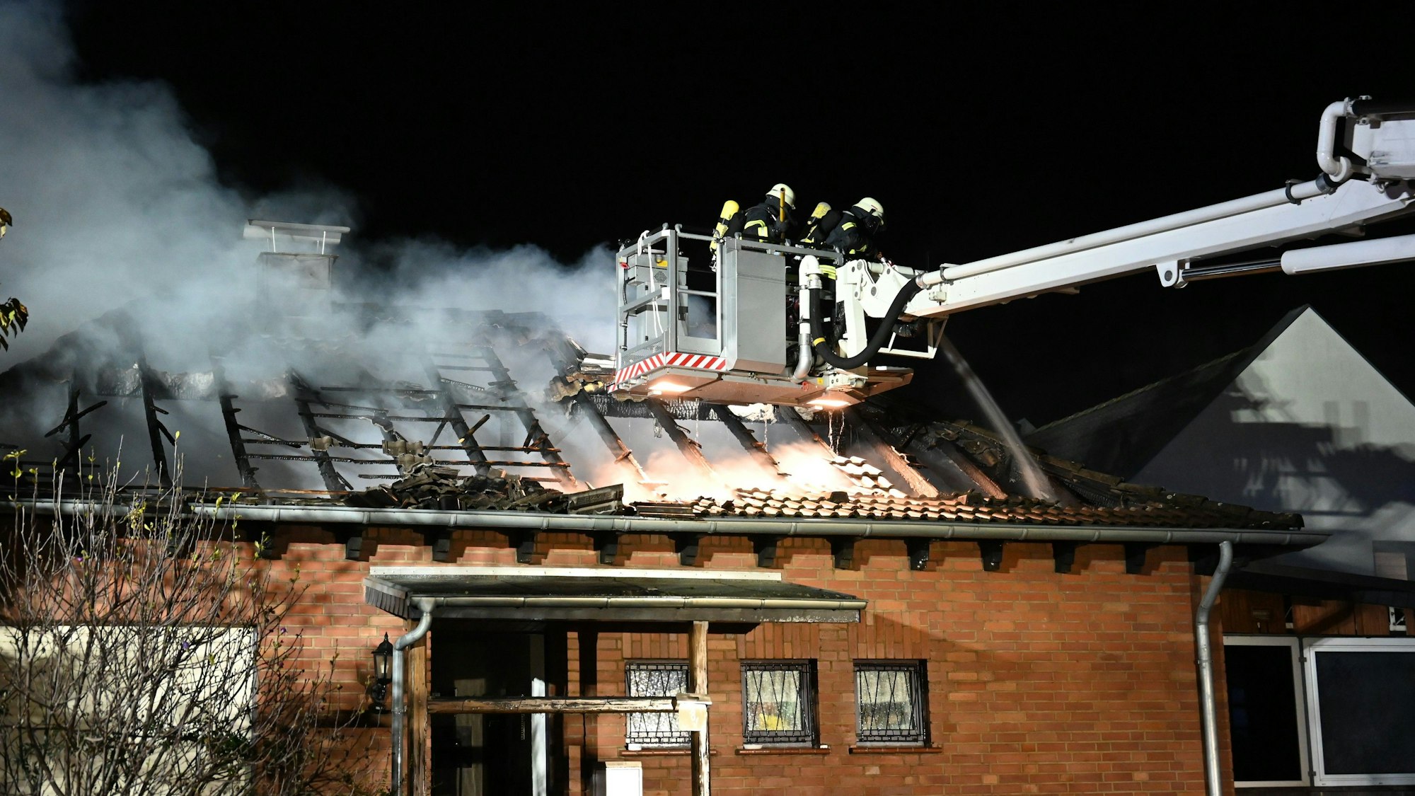 Feuerwehrleute auf einer Drehleiter löschen den Brand in einem Bungalow in Kerpen-Sindorf.
