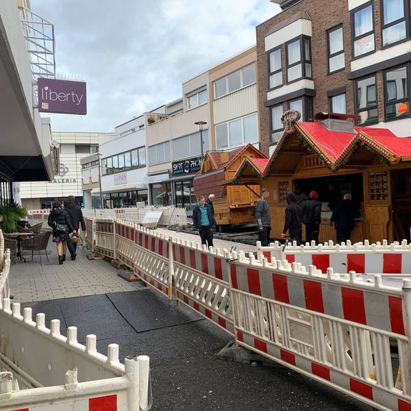 In der Berliner Straße in Euskirchen, die erneuert wird, stehen Bauzäune. Dahinter stellen mehrere Männer Verkaufsbuden für die Veranstaltung Winterzauber auf.