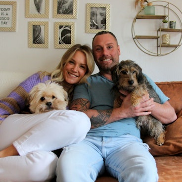 Eine Frau und ein Mann sitzen mit zwei Hunden auf einem Sofa.