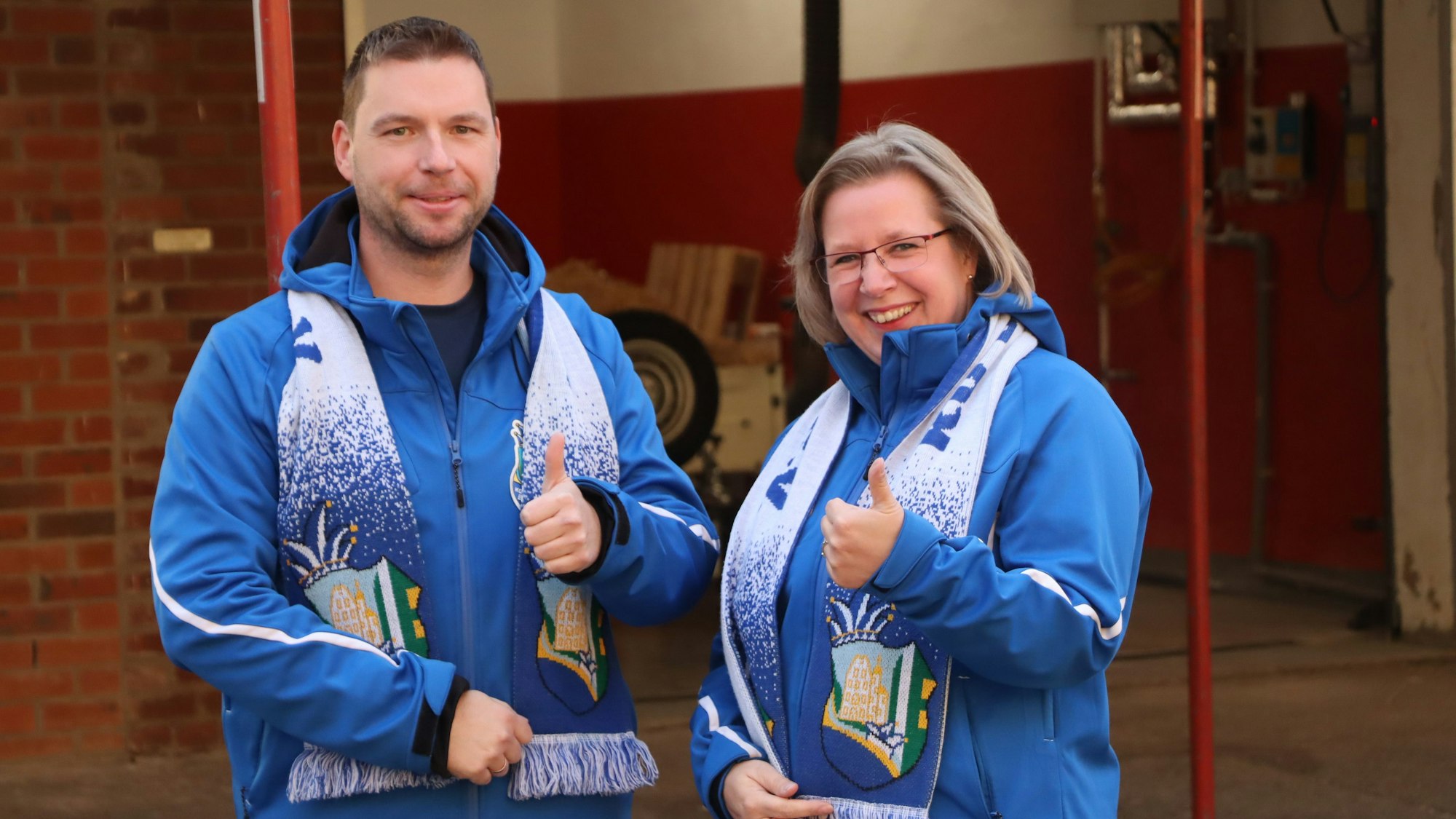 Ein Mann und eine Frau mit einem Schal der KG Blessem recken jeweils den linken Daumen in die Luft.