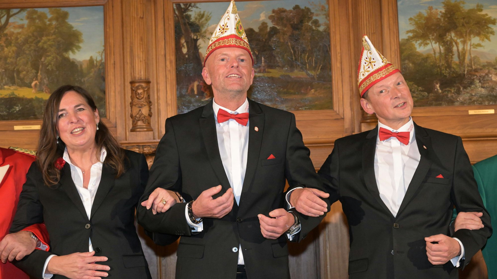 Drei Karnevalisten in schwarzen Anzügen schunkeln.