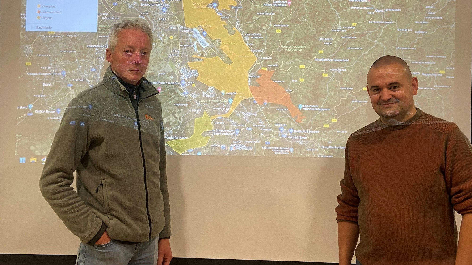 Zwei Männer stehen vor einer Leinwand, auf die eine Karte projiziert wird.