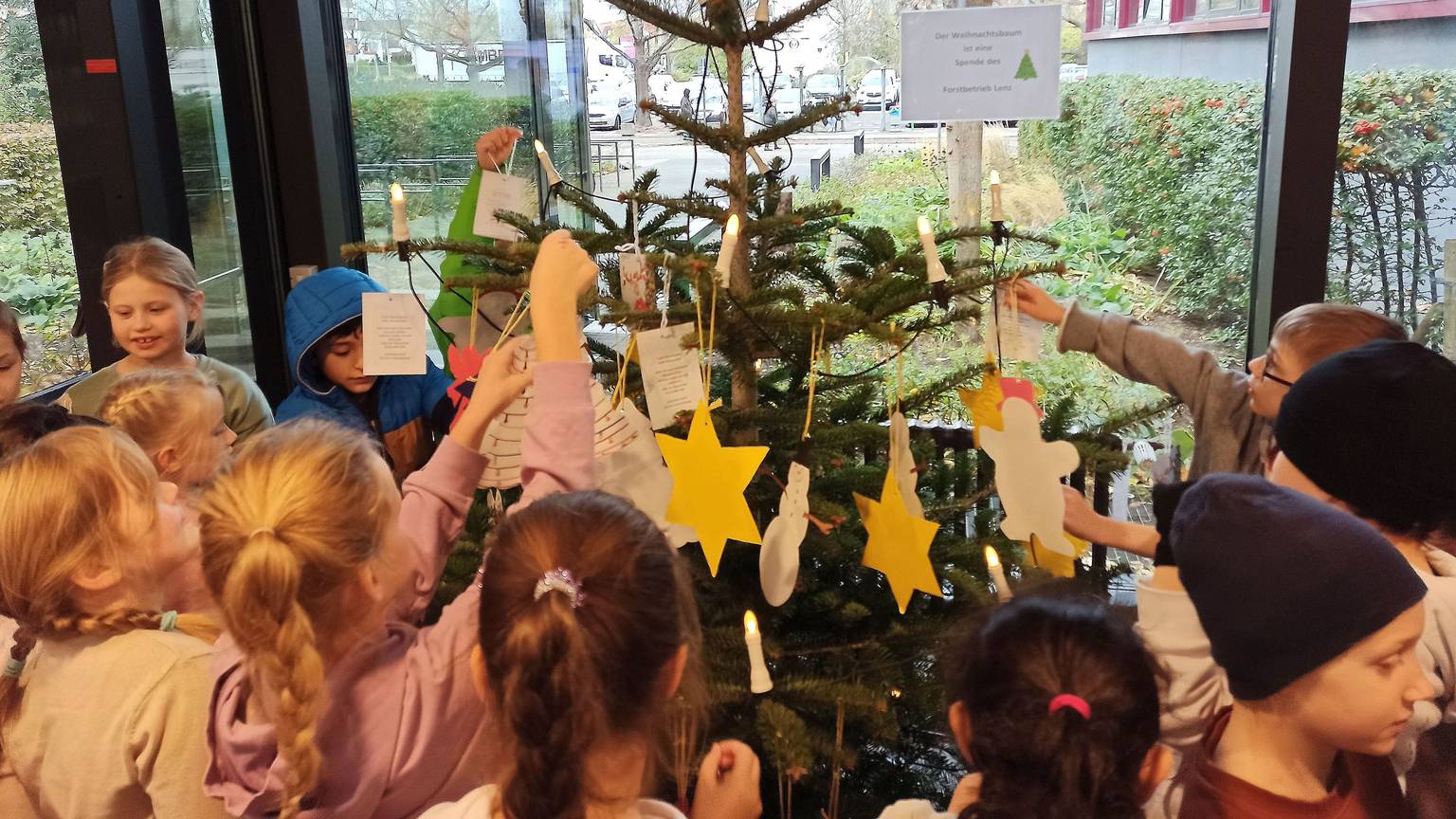 Kinder stehen um einen Weihnachtsbaum und schmücken ihn.