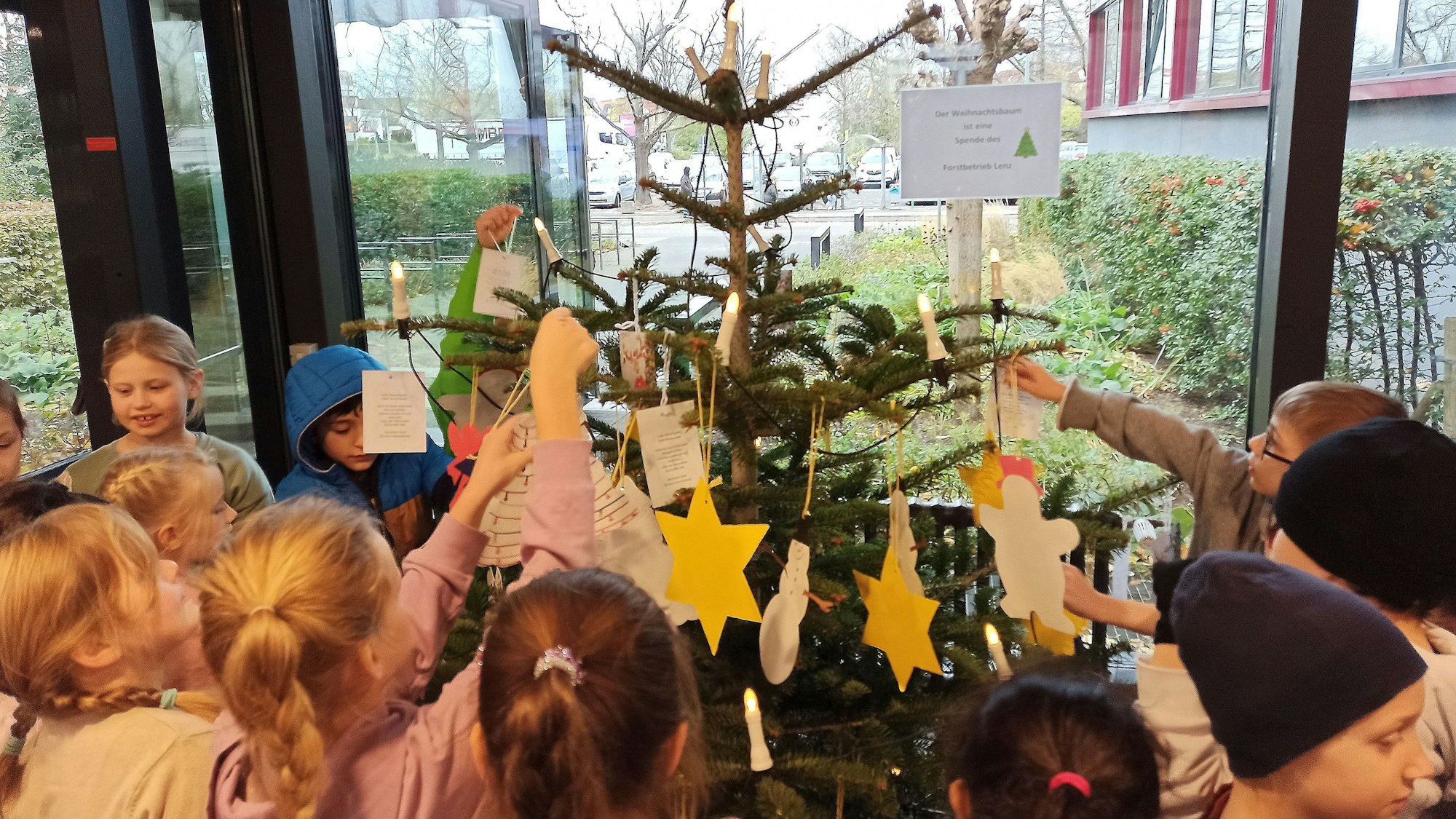 Kinder stehen um einen Weihnachtsbaum und schmücken ihn.