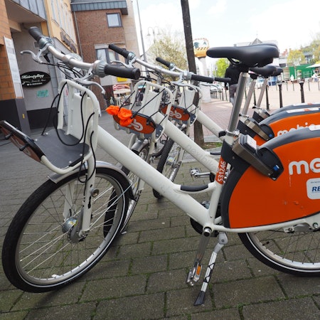 Zu sehen sind weiße Mietfahrräder mit dem orangefarbenen Schriftzug Mobic.