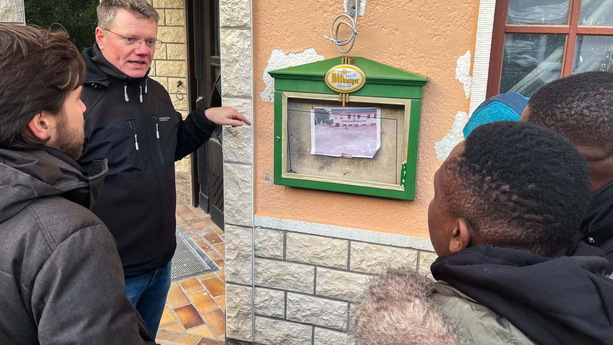 Das Bild zeigt Karl Kreuzberg vor der Gaststätte in Schweinheim. Menschen aus Ghana hören ihm zu.