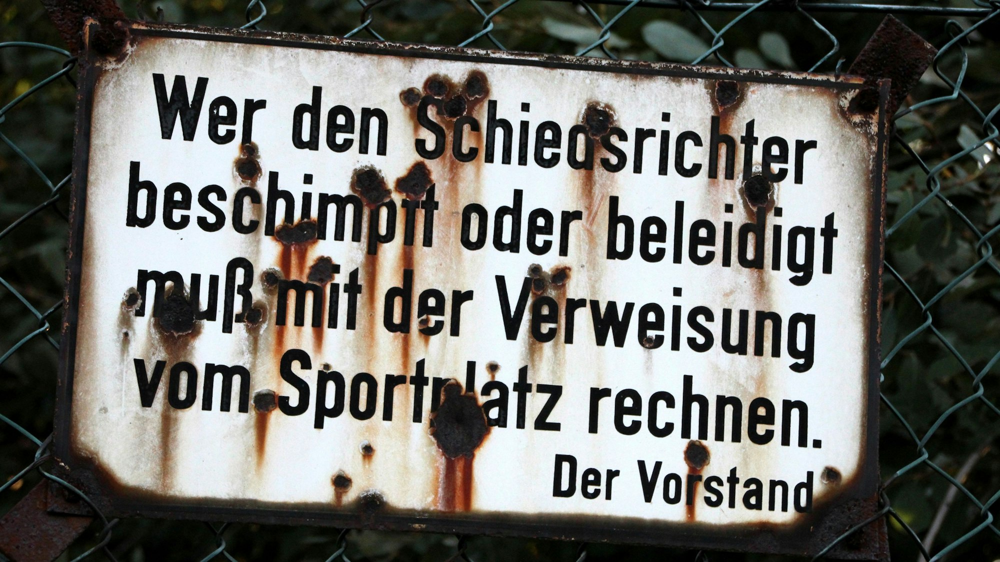 Auf einem von Rost zerfressenen Schild steht: „Wer den Schiedsrichter beschimpft oder beleidigt muß mit der Verweisung vom Sportplatz rechnen. Der Vorstand“