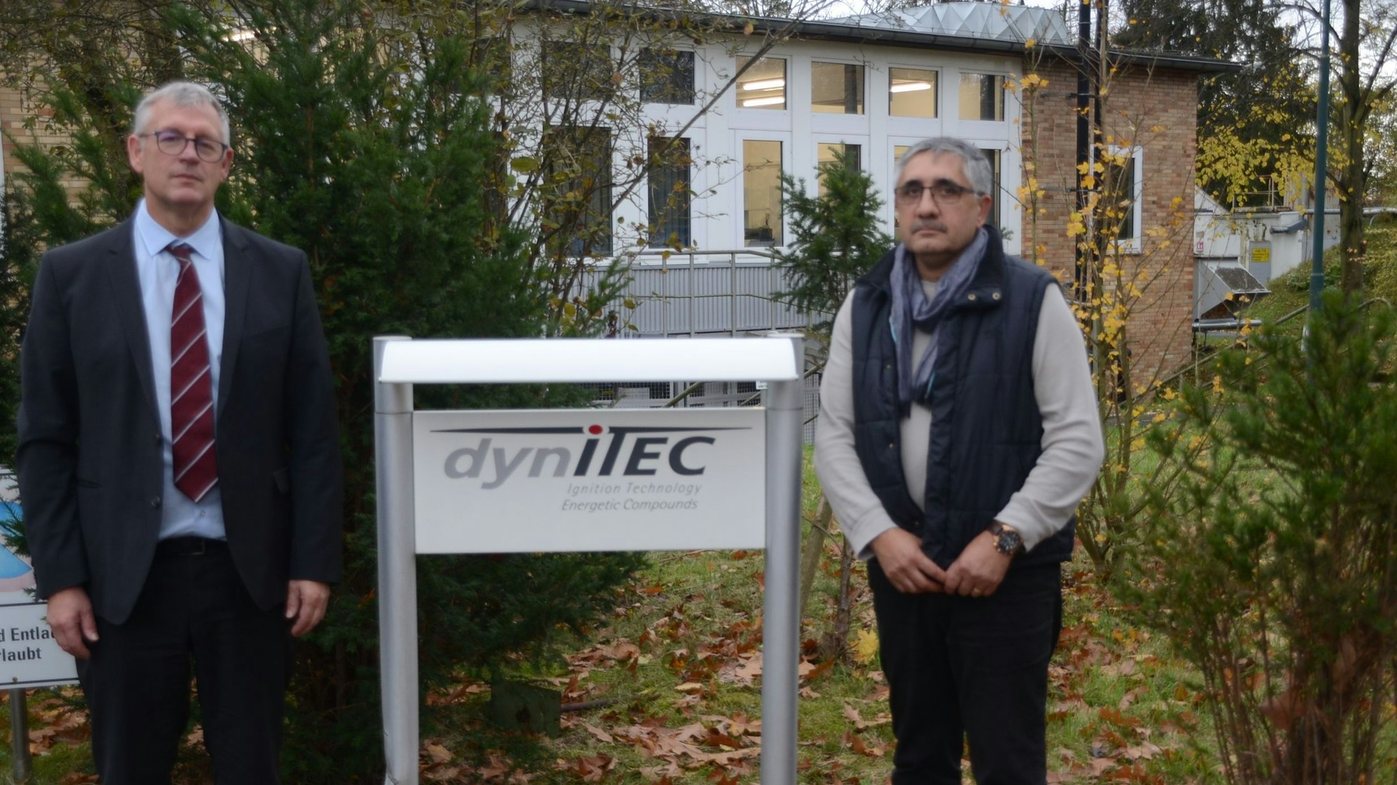 Zwei Männer stehen neben einem Firmenschild.