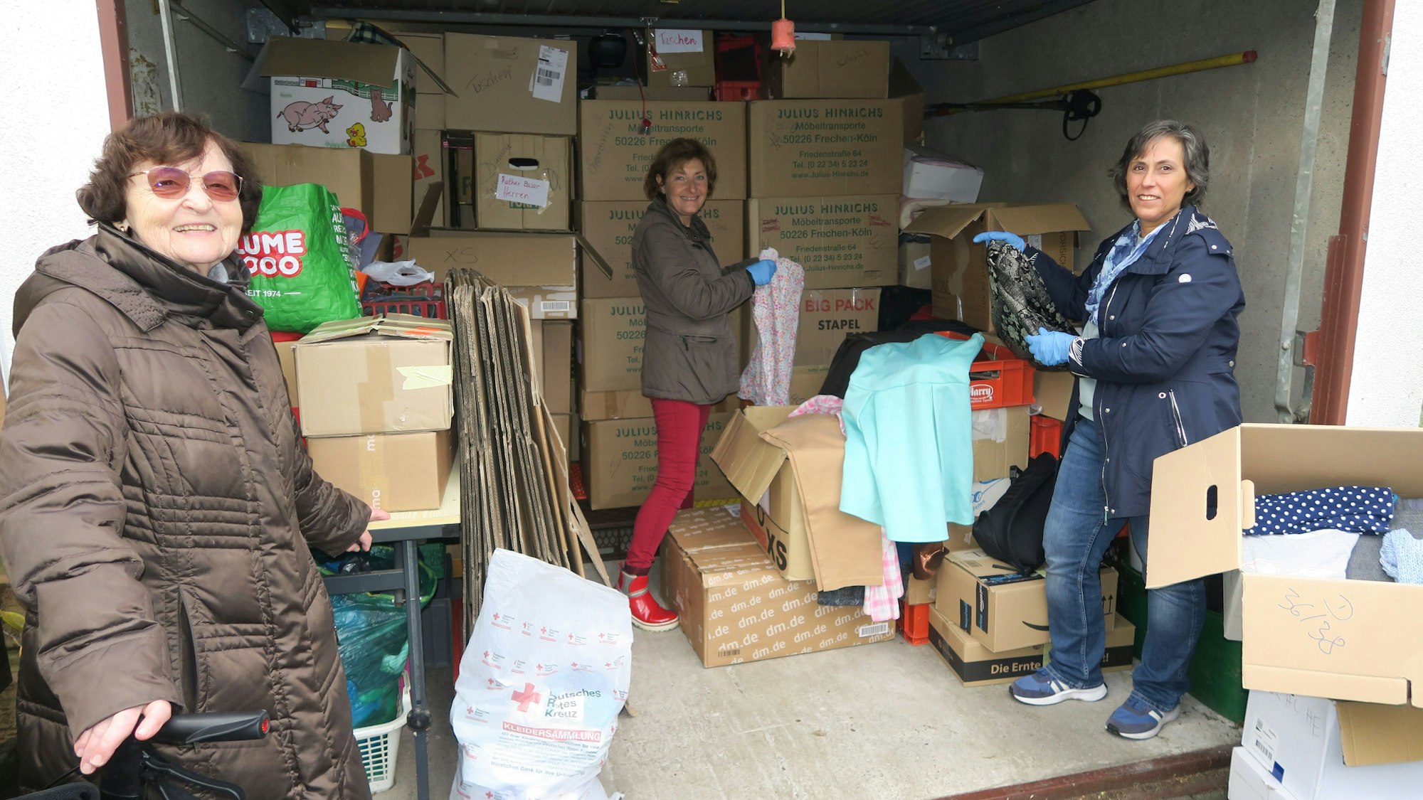 Drei Frauen stehen in einer Garage, die voll ist mit Kartons.