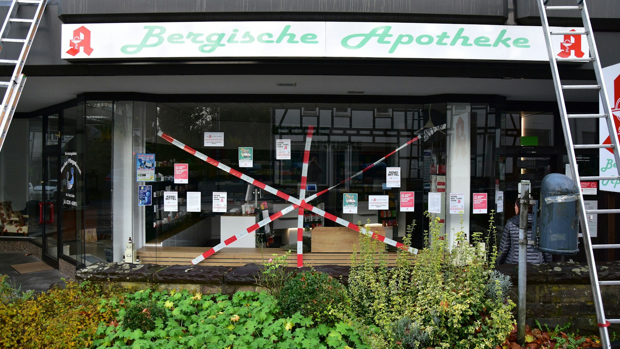 Bergische Apotheke in Much. Rotweißes Flatterband ist kreuz und quer vor das Schaufenster gespannt.